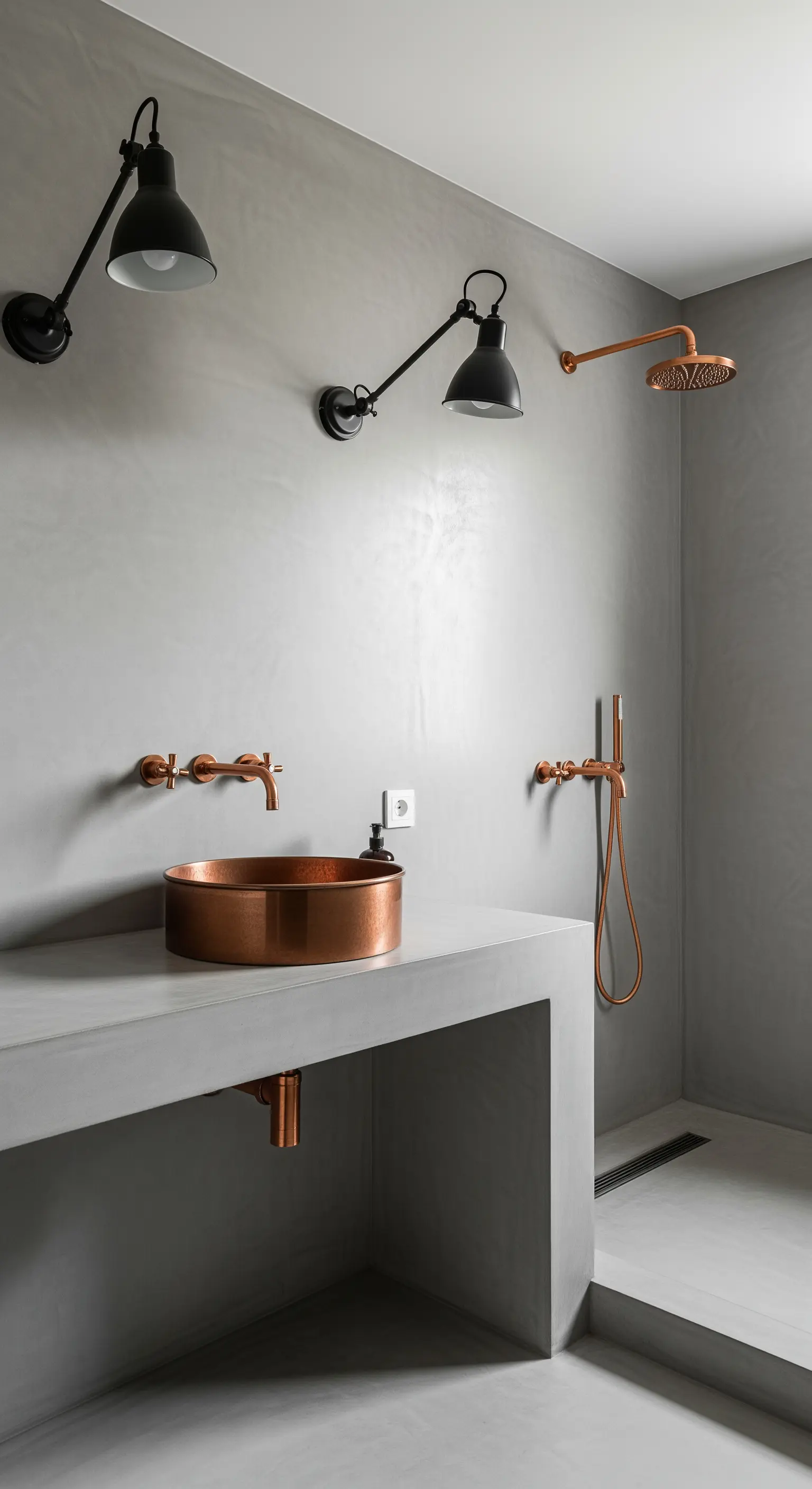 Bagno in cemento levigato con lavabo in rame e applique nere industriali.