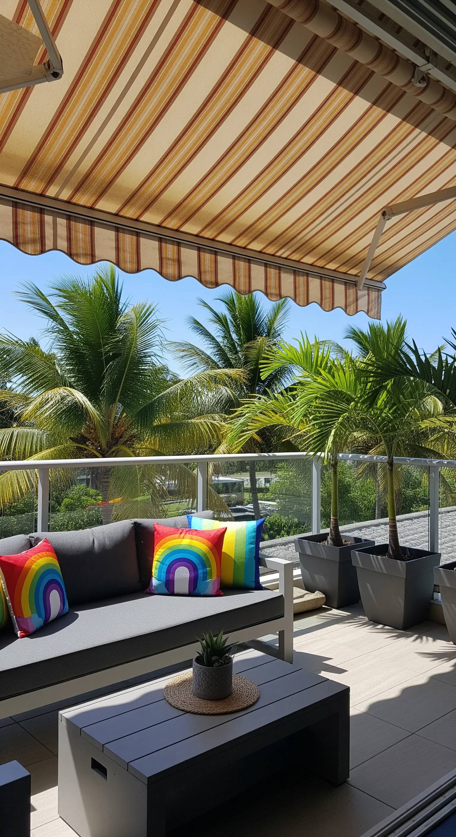 Divano grigio da esterno con cuscini arcobaleno e piante di palma in vasi grigi.