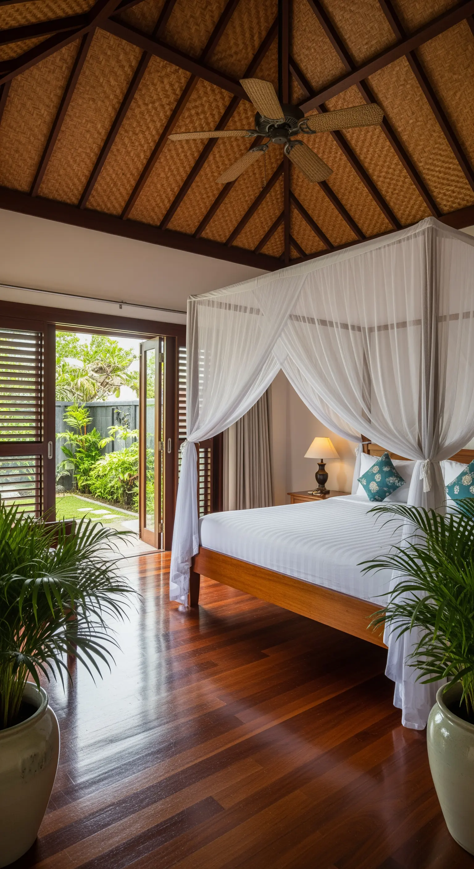 Letto a baldacchino in legno con zanzariera bianca che si affaccia su un giardino tropicale.