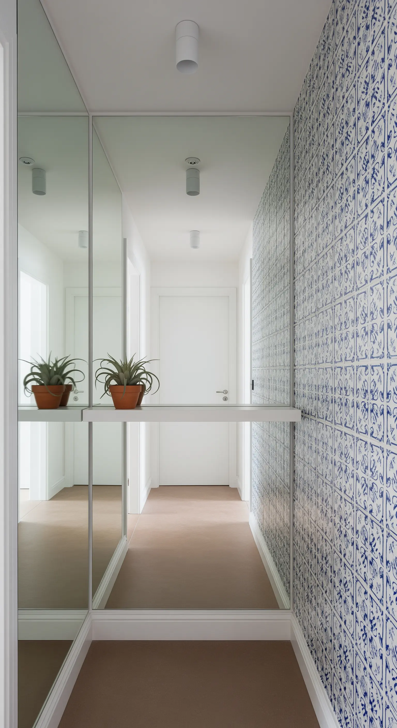Corridoio stretto con una parete a specchio che riflette una parete a maiolica blu e bianca.