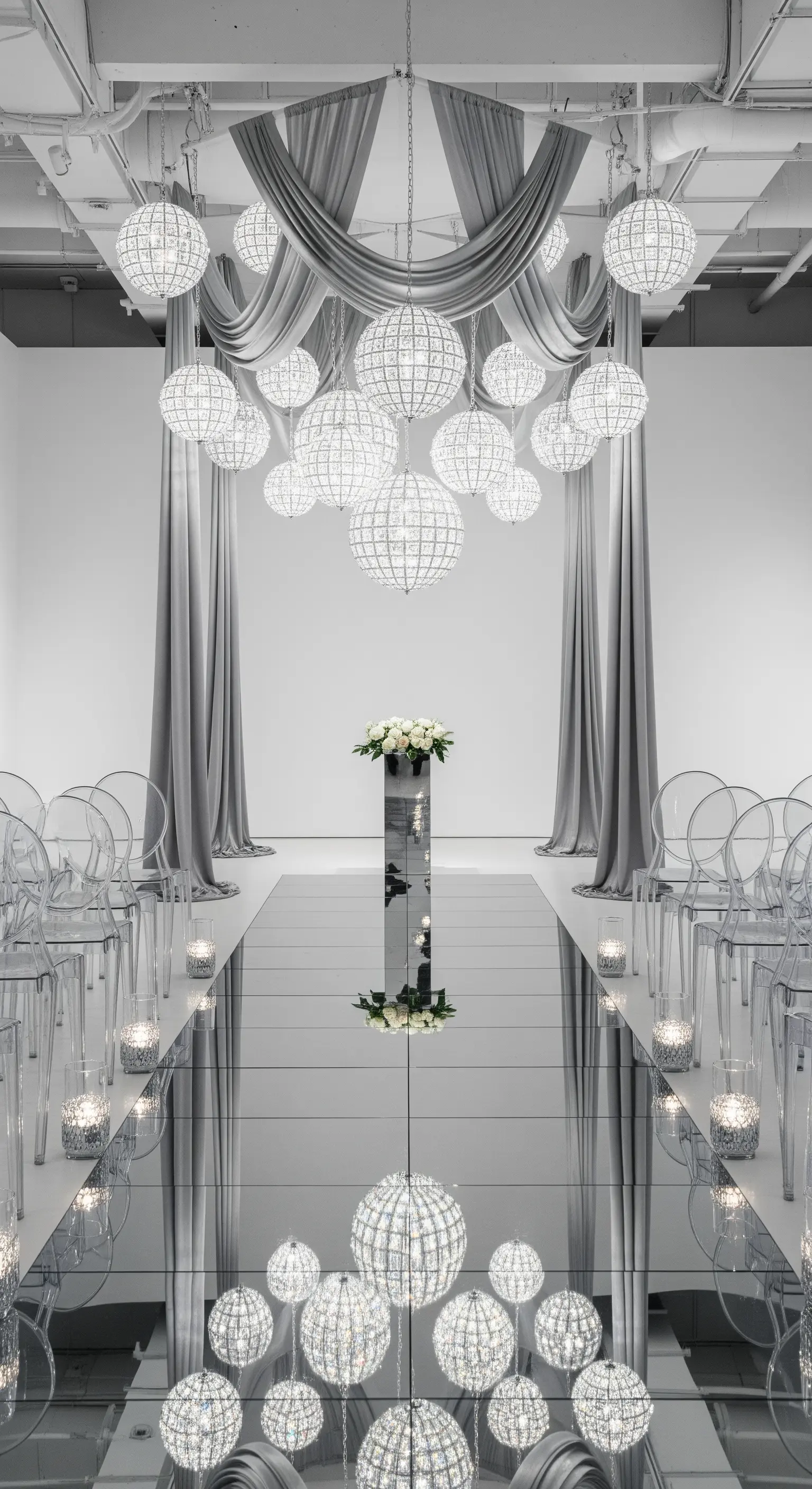 Navata a specchio con chandelier sferici sospesi e sedie trasparenti in un ambiente total white.