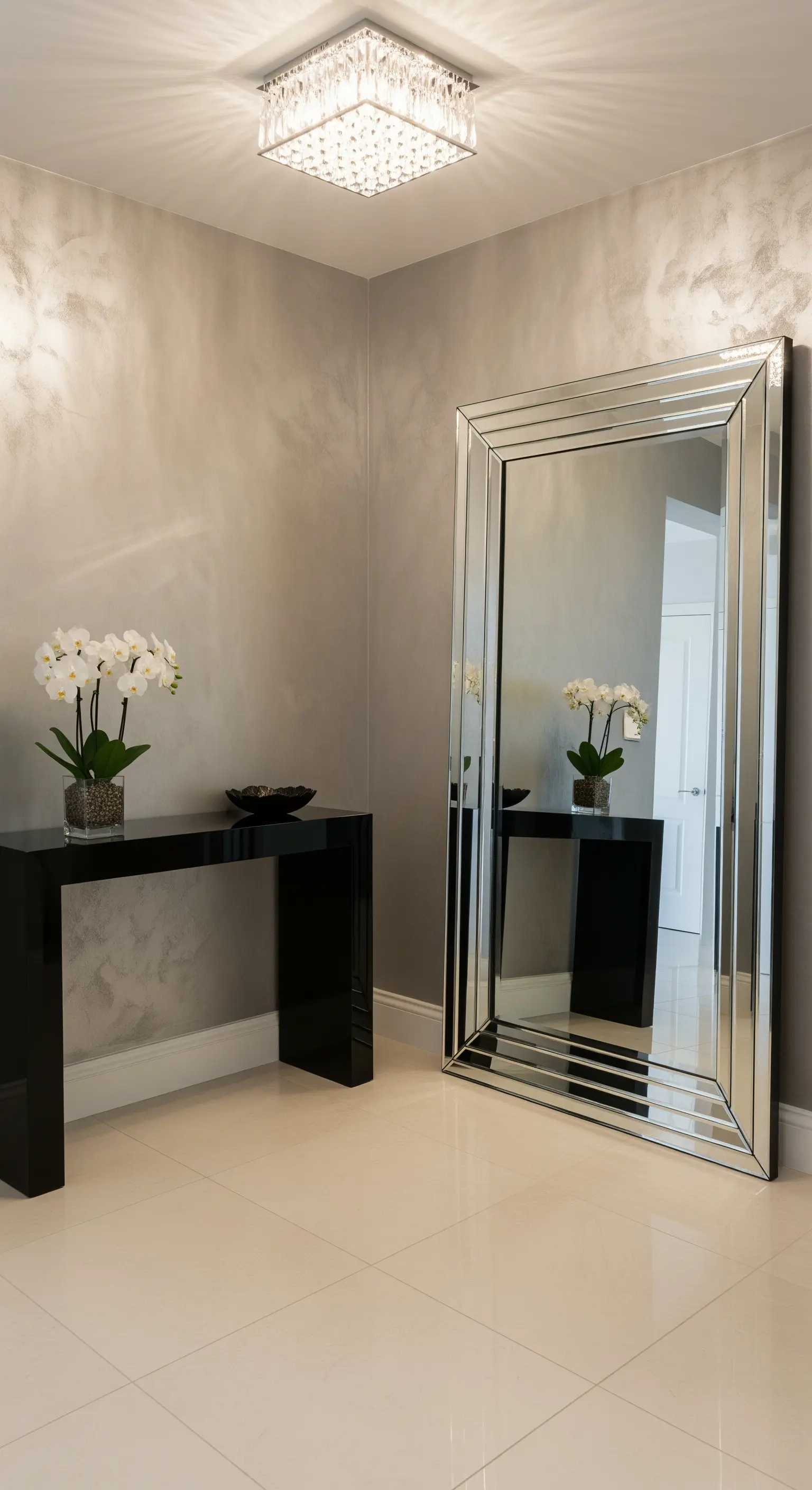 Ingresso elegante con grande specchio dalla cornice sfaccettata e consolle nera laccata.