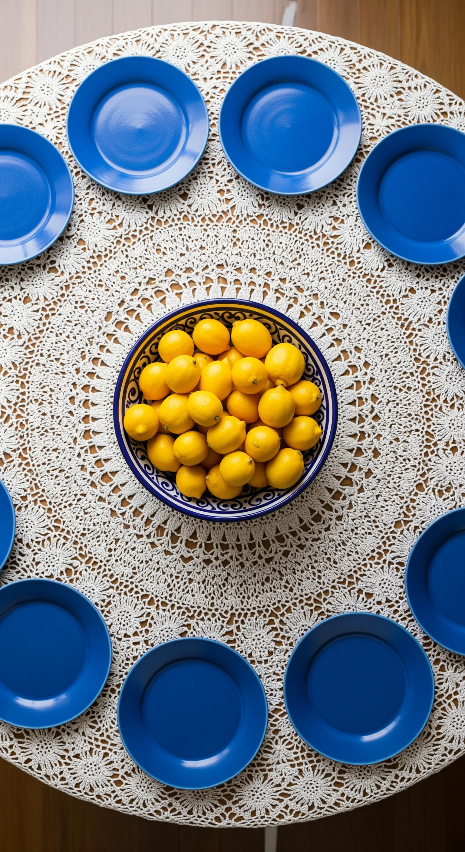 Tavolo rotondo visto dall'alto con piatti blu disposti a cerchio e ciotola di limoni.