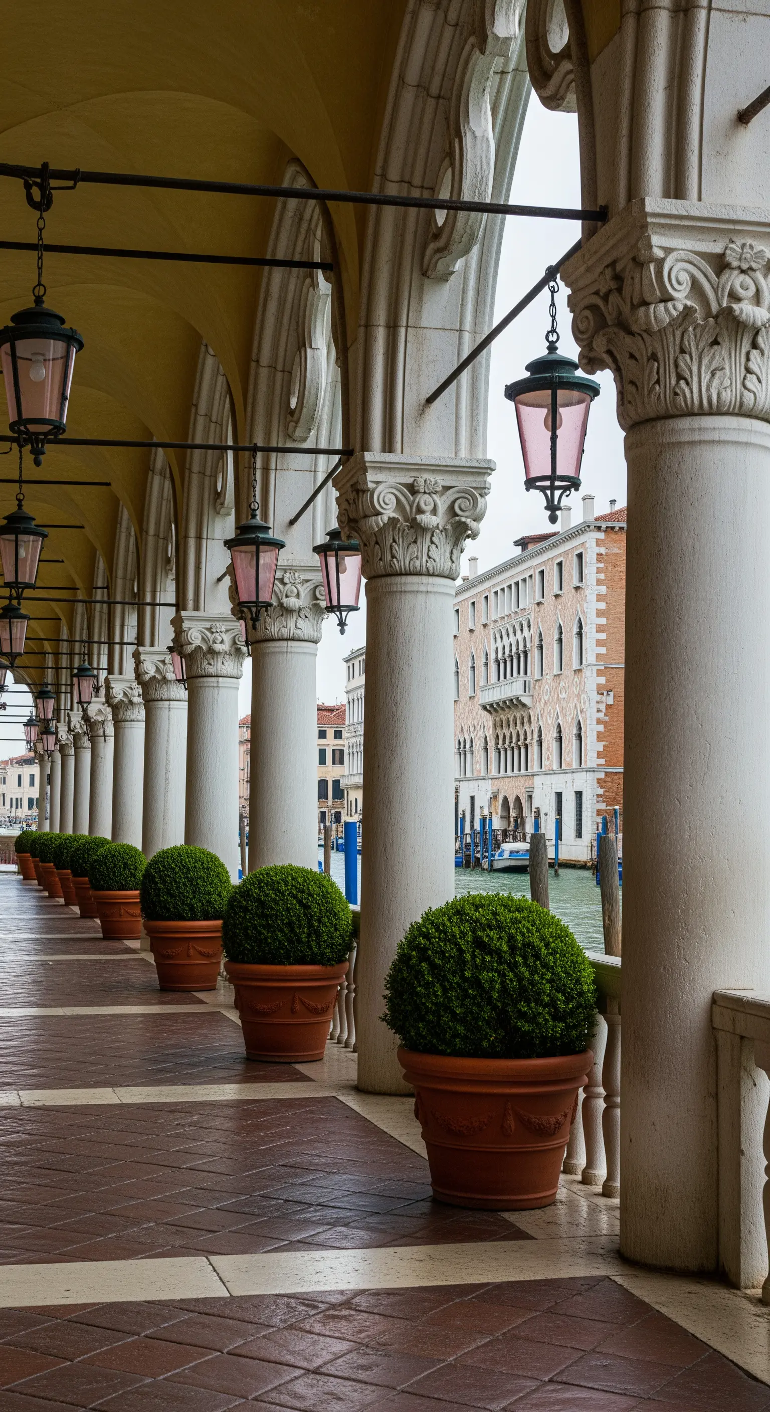 Lungo porticato con colonne bianche e una fila di vasi in terracotta con piante sferiche.