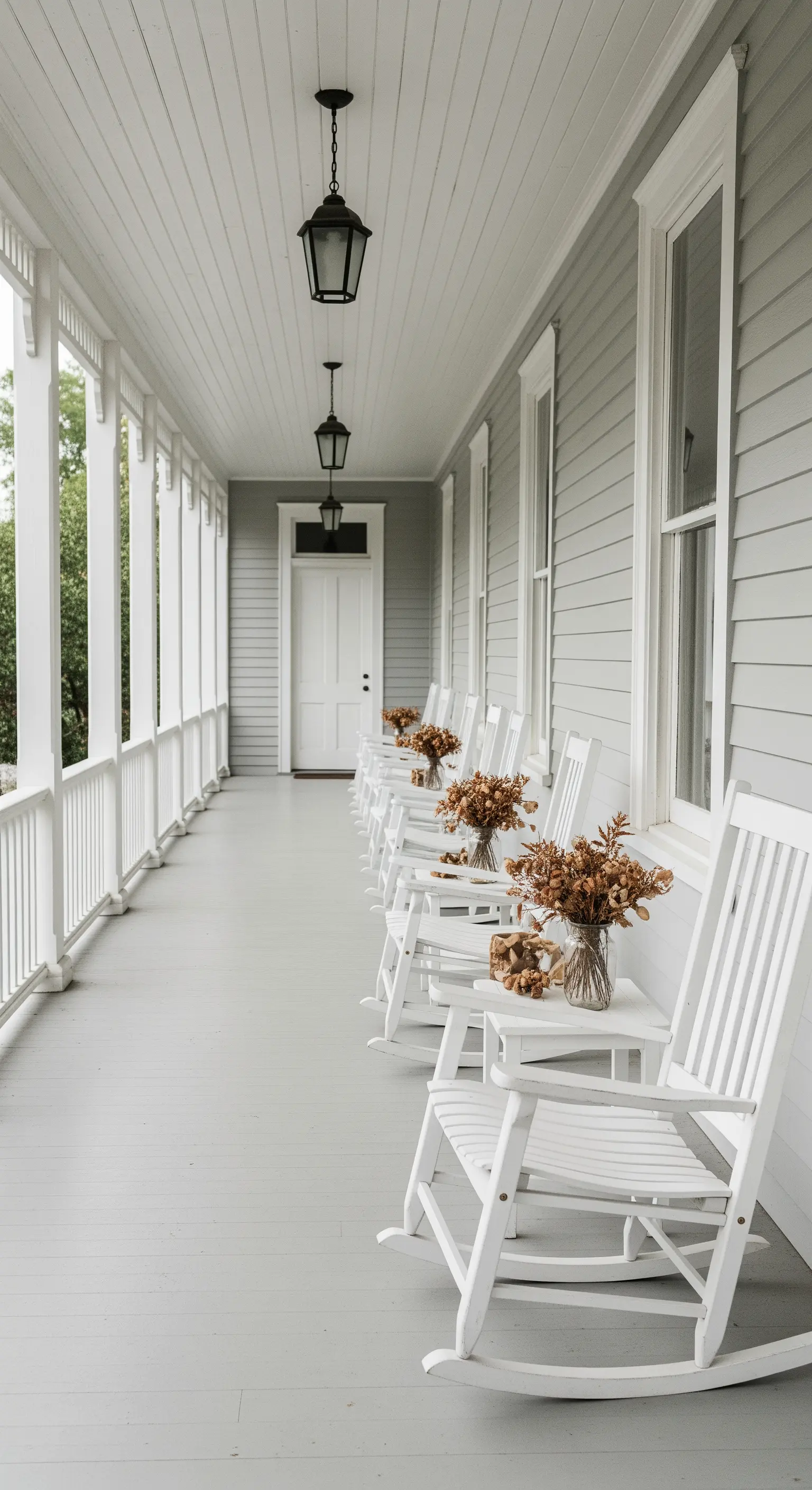 Lungo portico bianco con una fila ordinata di sedie a dondolo e piccole composizioni floreali.
