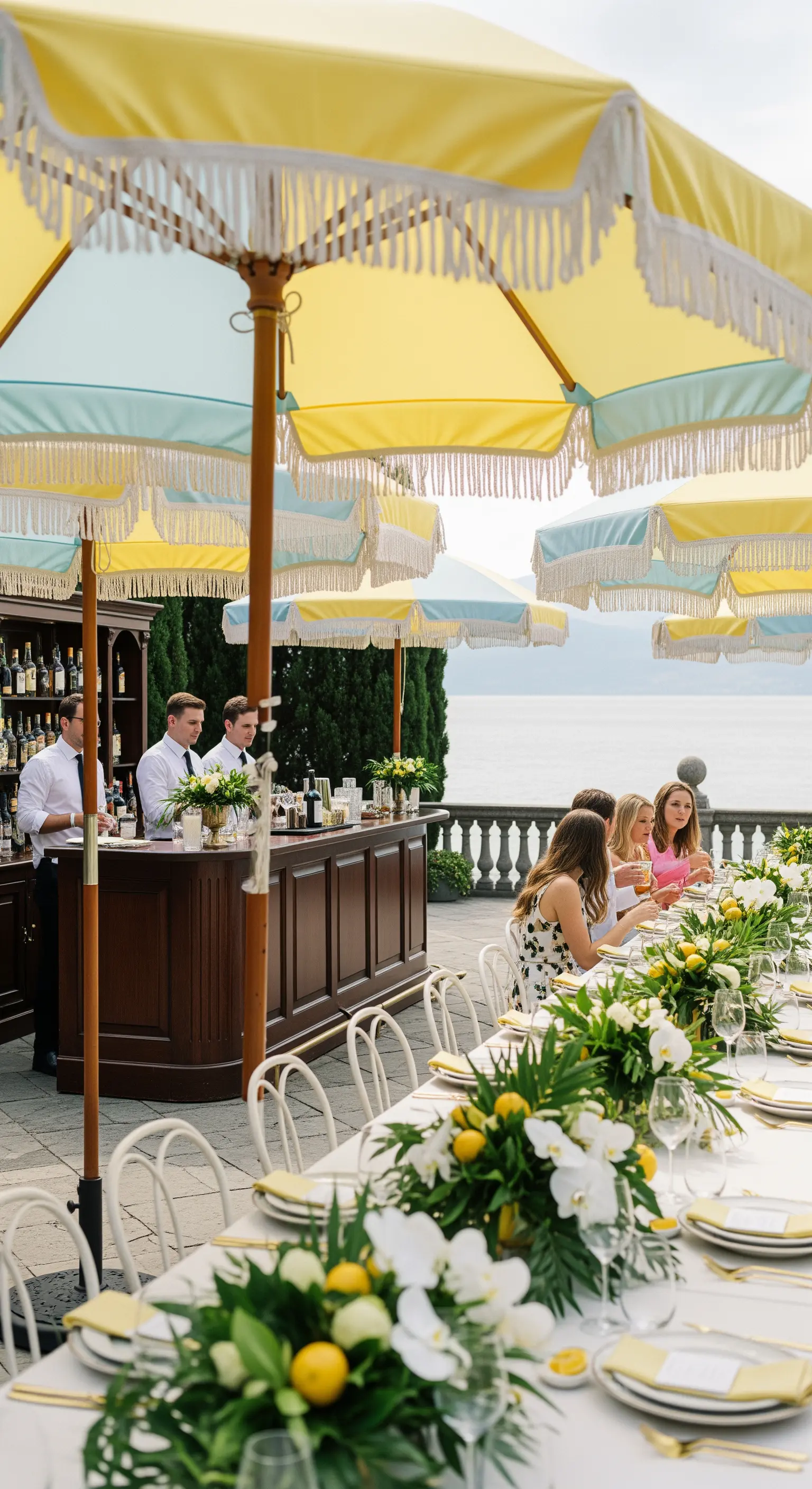 Tavolata elegante vista lago con ombrelloni gialli e centrotavola di limoni e orchidee bianche