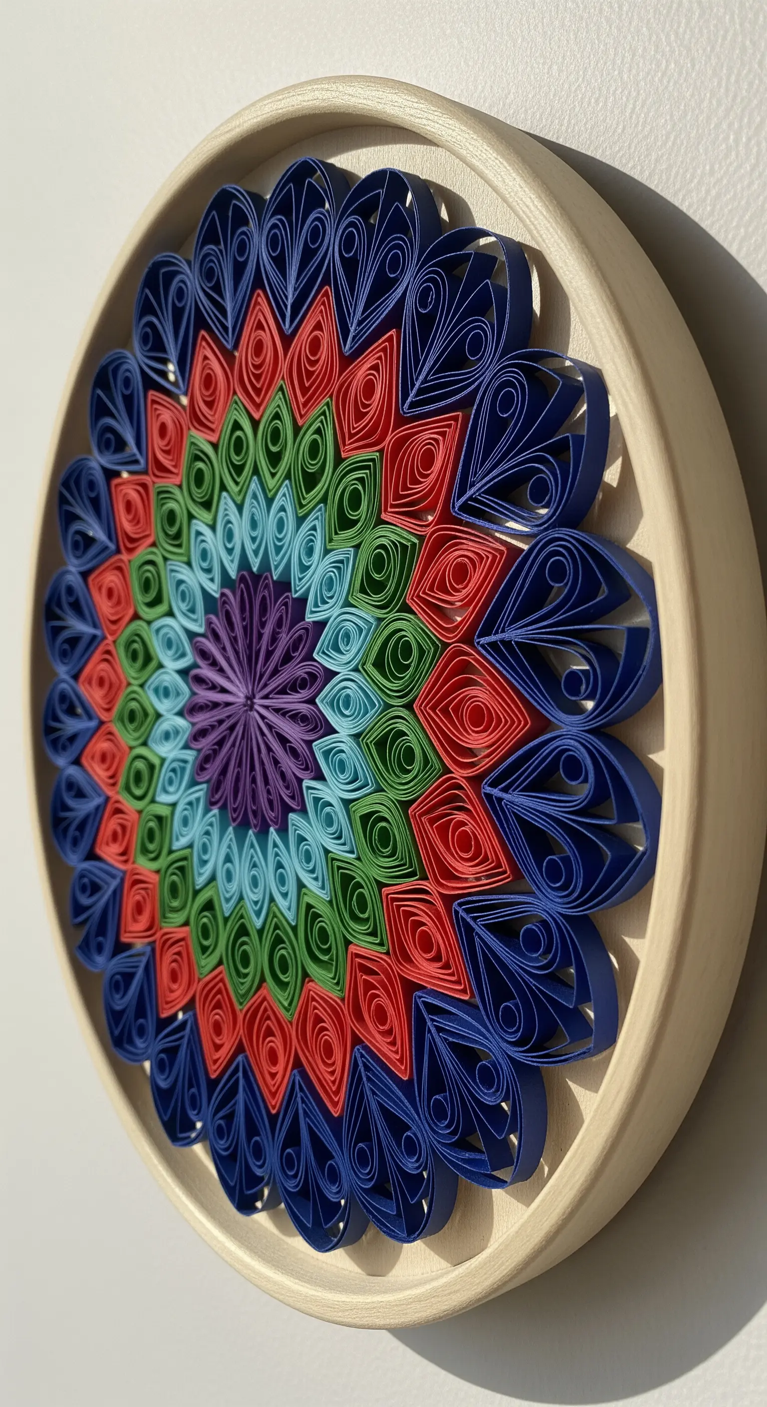 Decorazione murale circolare con complessi motivi quilling multicolore in una cornice di legno chiaro.