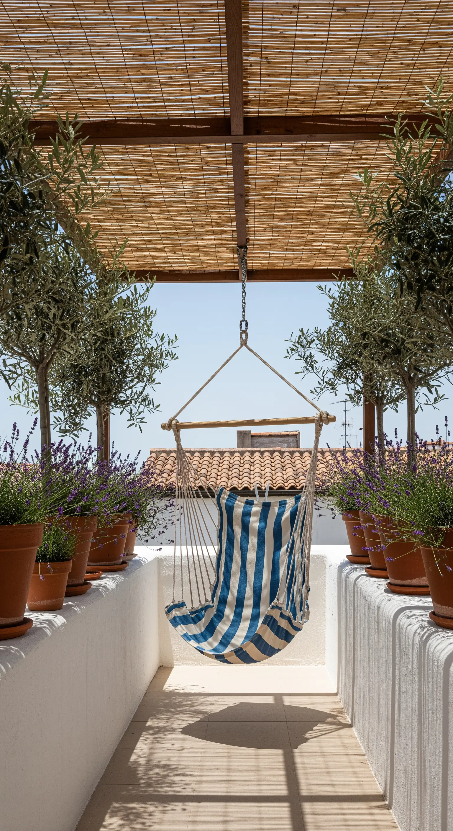 Amaca a righe sotto una pergola in bambù, tra vasi di ulivi e lavanda.