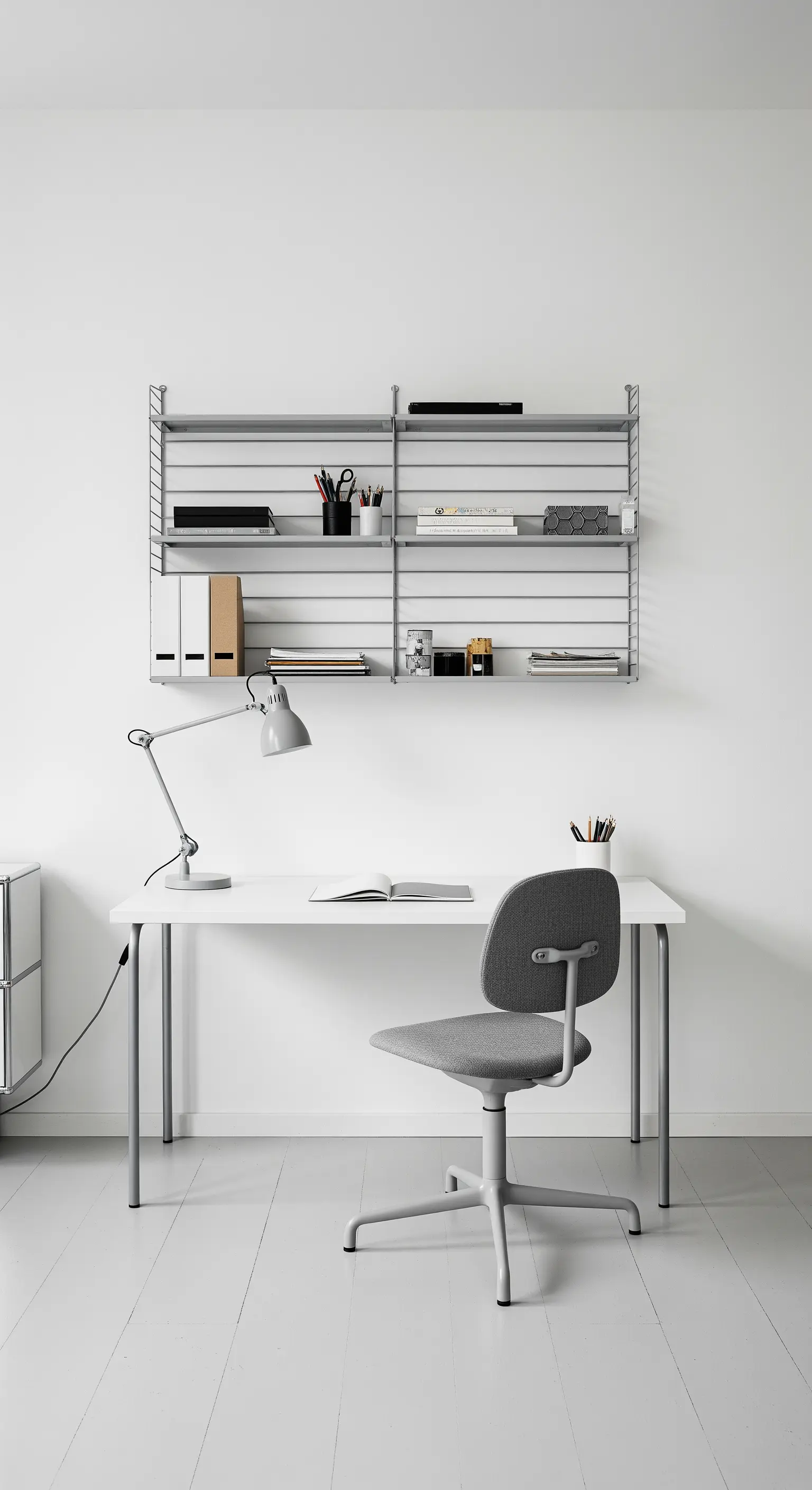 Scrivania bianca con sedia grigia sotto un sistema di scaffalature a parete String grigio.