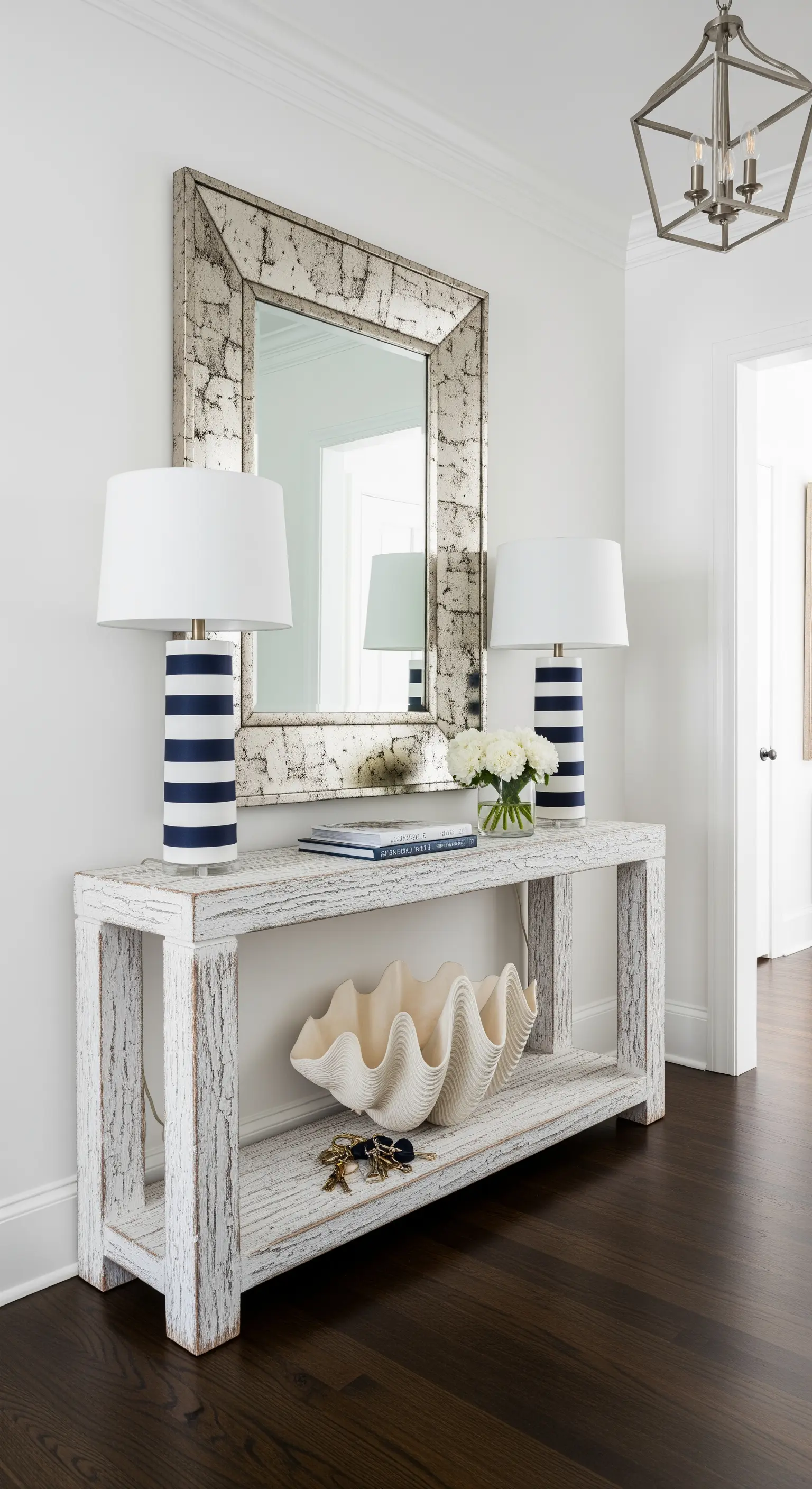 Consolle in legno bianco texturizzato con lampade a righe e una grande conchiglia decorativa.