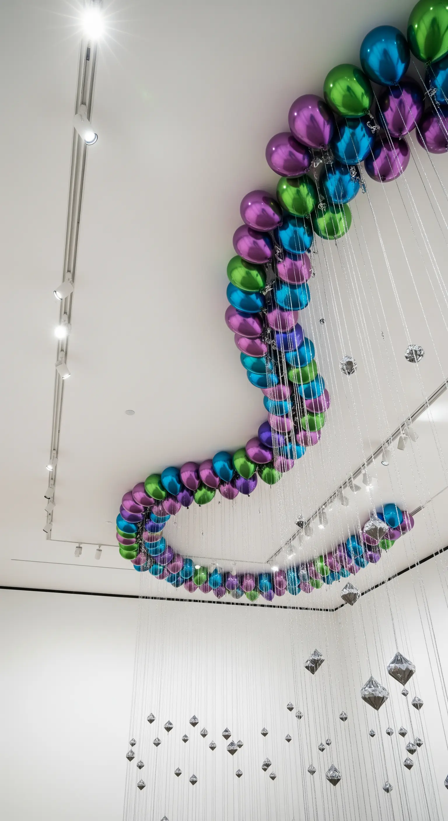Una lunga installazione a serpente fatta di palloncini metallizzati colorati sul soffitto bianco.