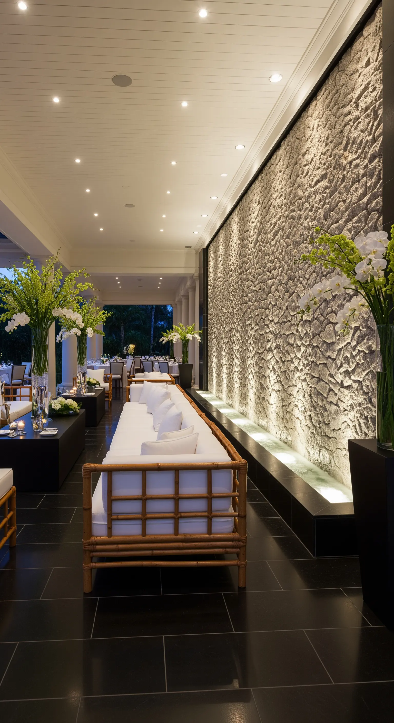 Lunga parete d'acqua testurizzata illuminata dal basso in una veranda elegante con divani in bambù.