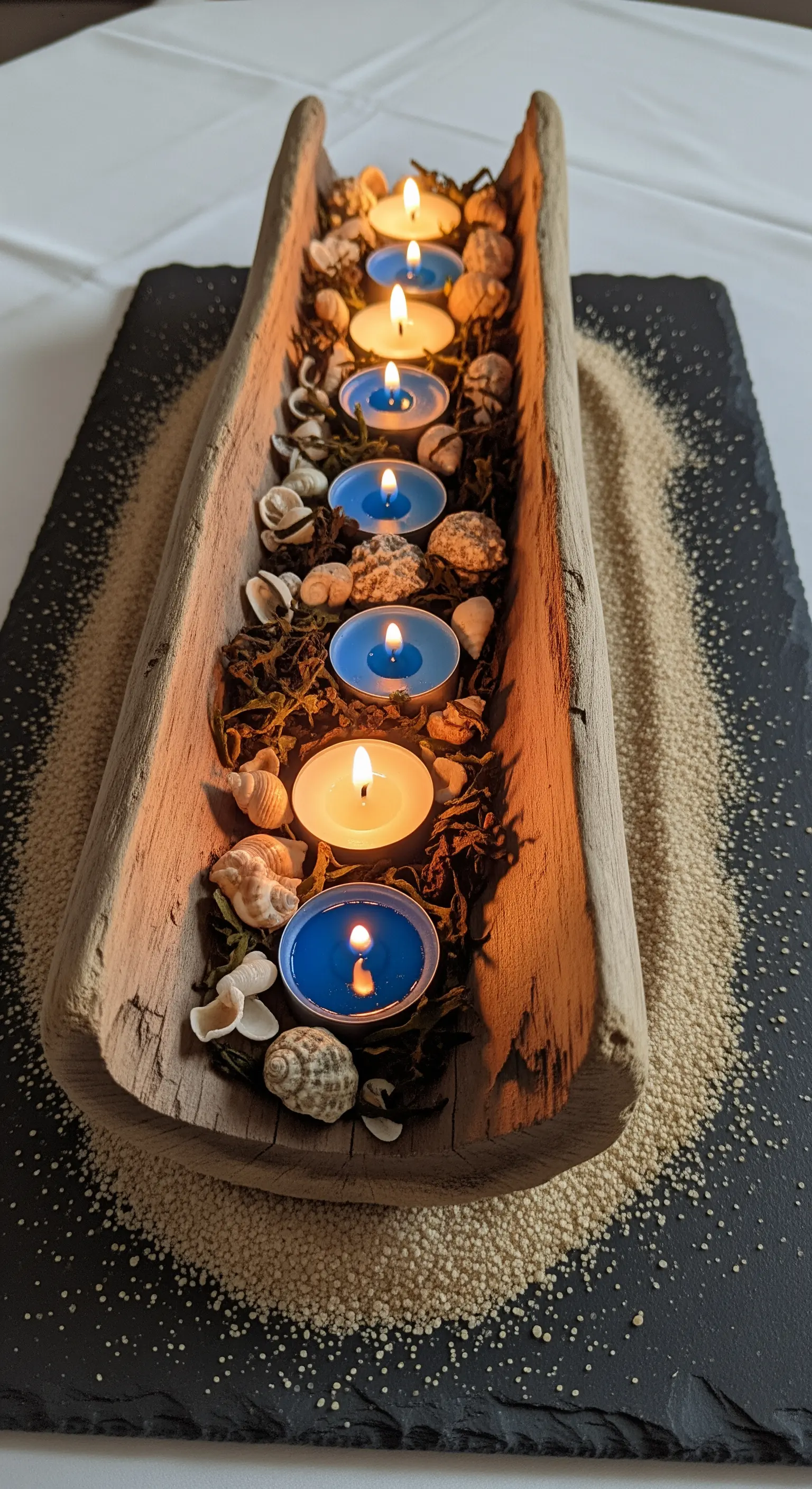 Legno levigato usato come portacandele con lumini blu e bianchi, conchiglie e sabbia.