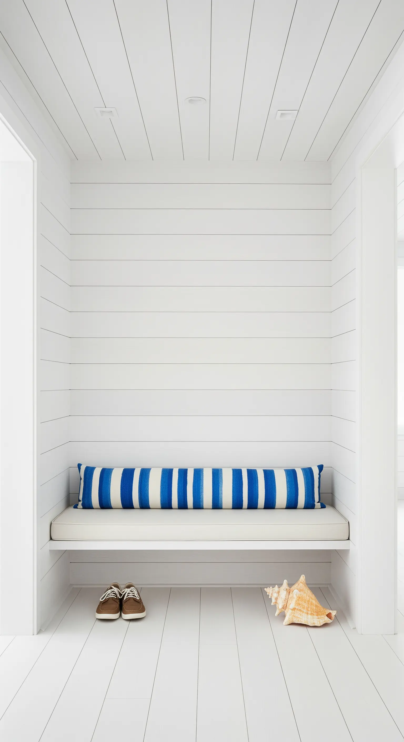 Nicchia total white con panca integrata e un lungo cuscino a righe blu.