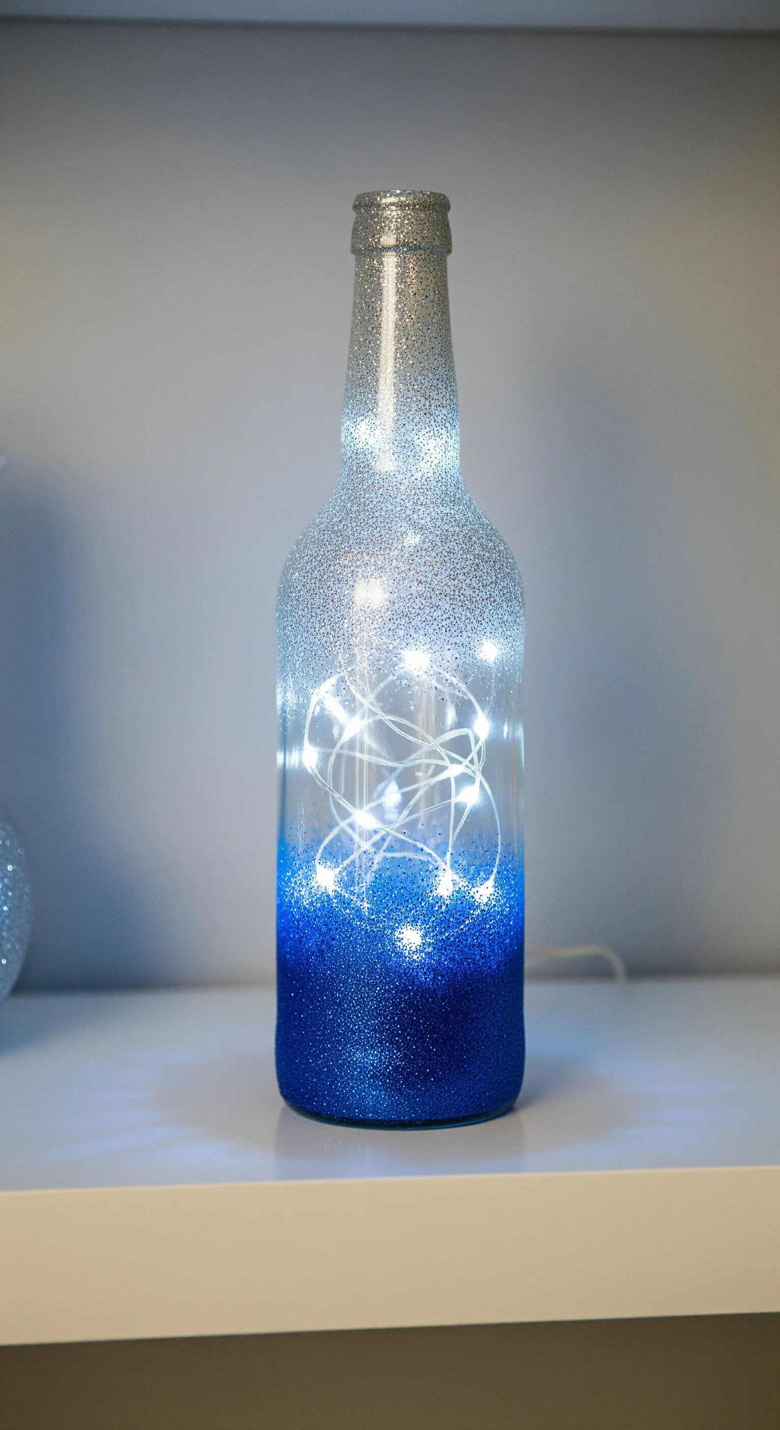Bottiglia di vetro con glitter sfumato da blu ad argento, illuminata dall'interno.