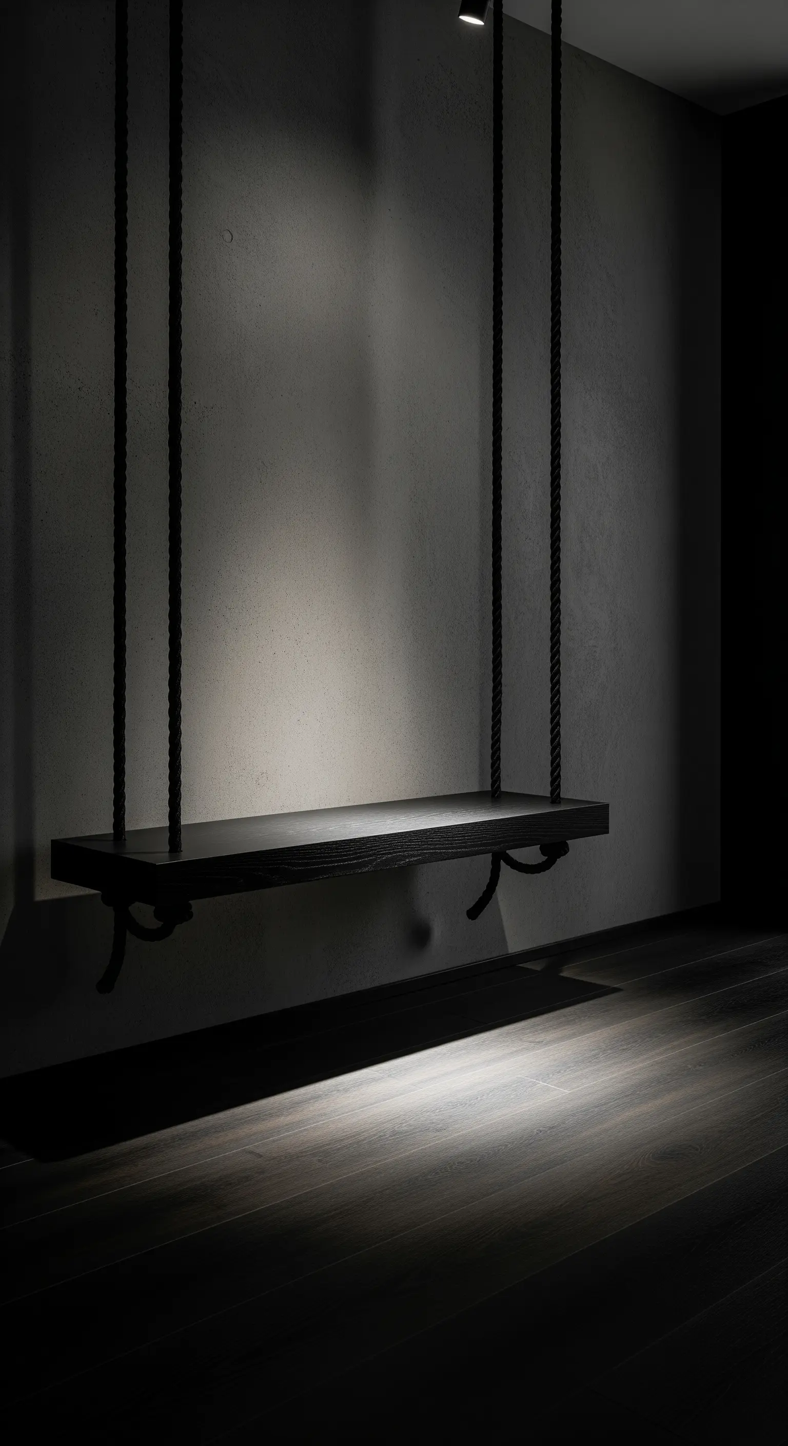 Panca sospesa nera con corde nere in una stanza buia, illuminata dall'alto.