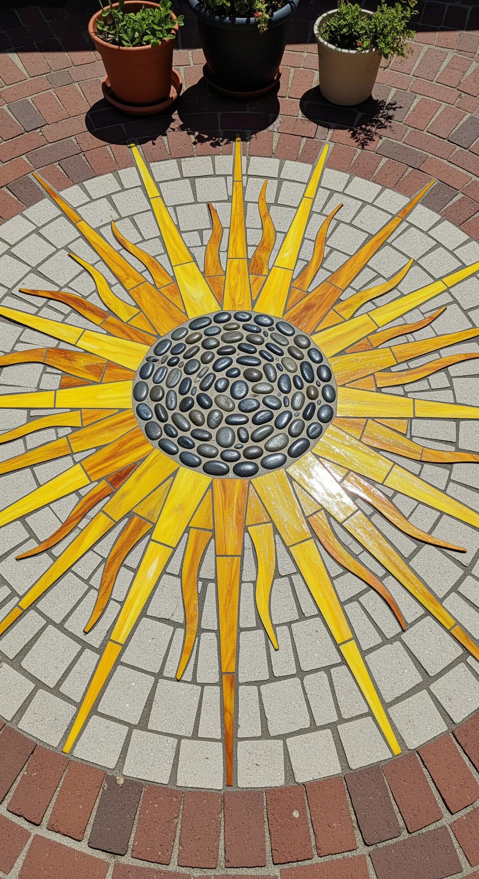 Grande mosaico a forma di sole con centro di ciottoli, incastonato in una pavimentazione di mattoni.