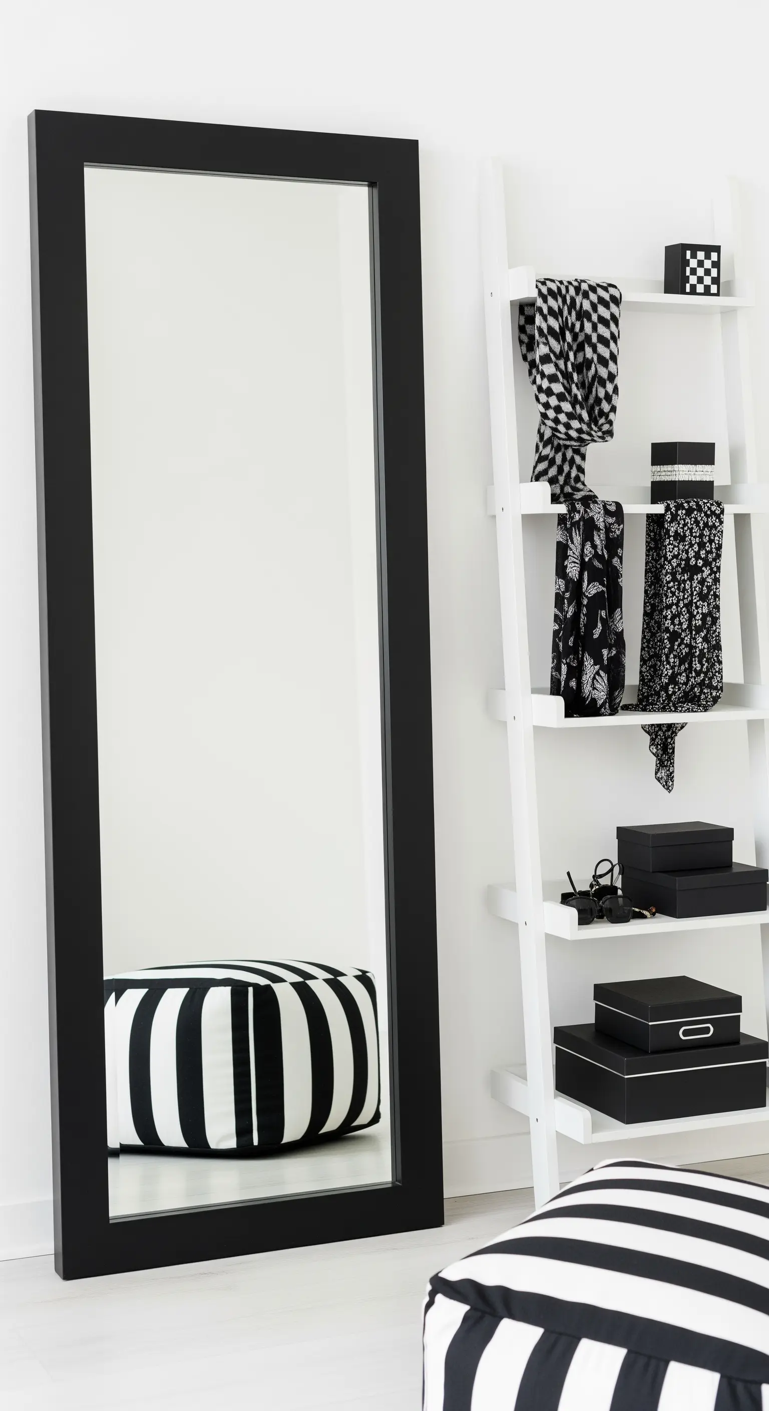 Grande specchio con cornice nera appoggiato al muro, con pouf a righe.