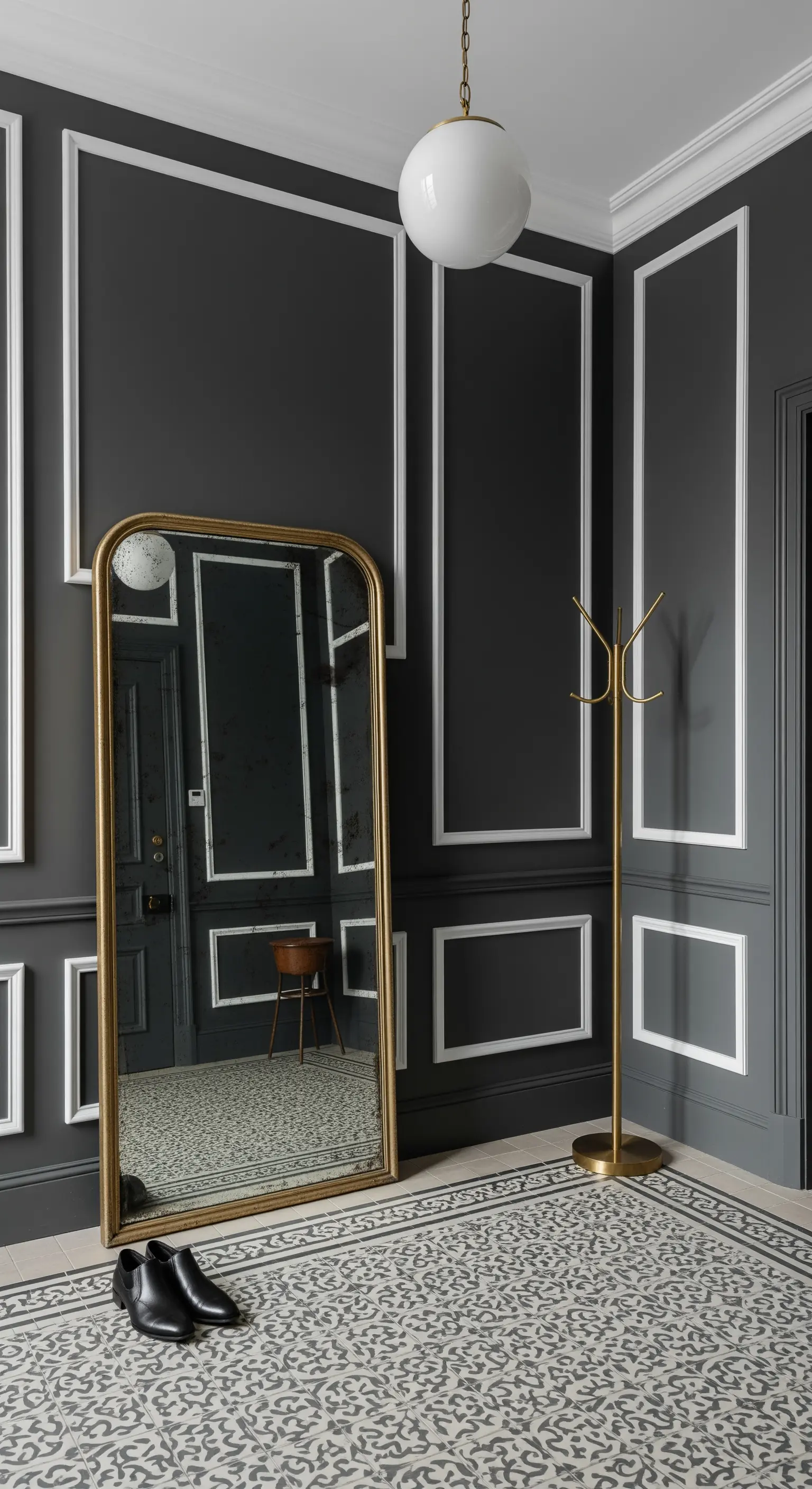 Ingresso grigio scuro con boiserie bianca a contrasto e specchio dorato appoggiato a terra.