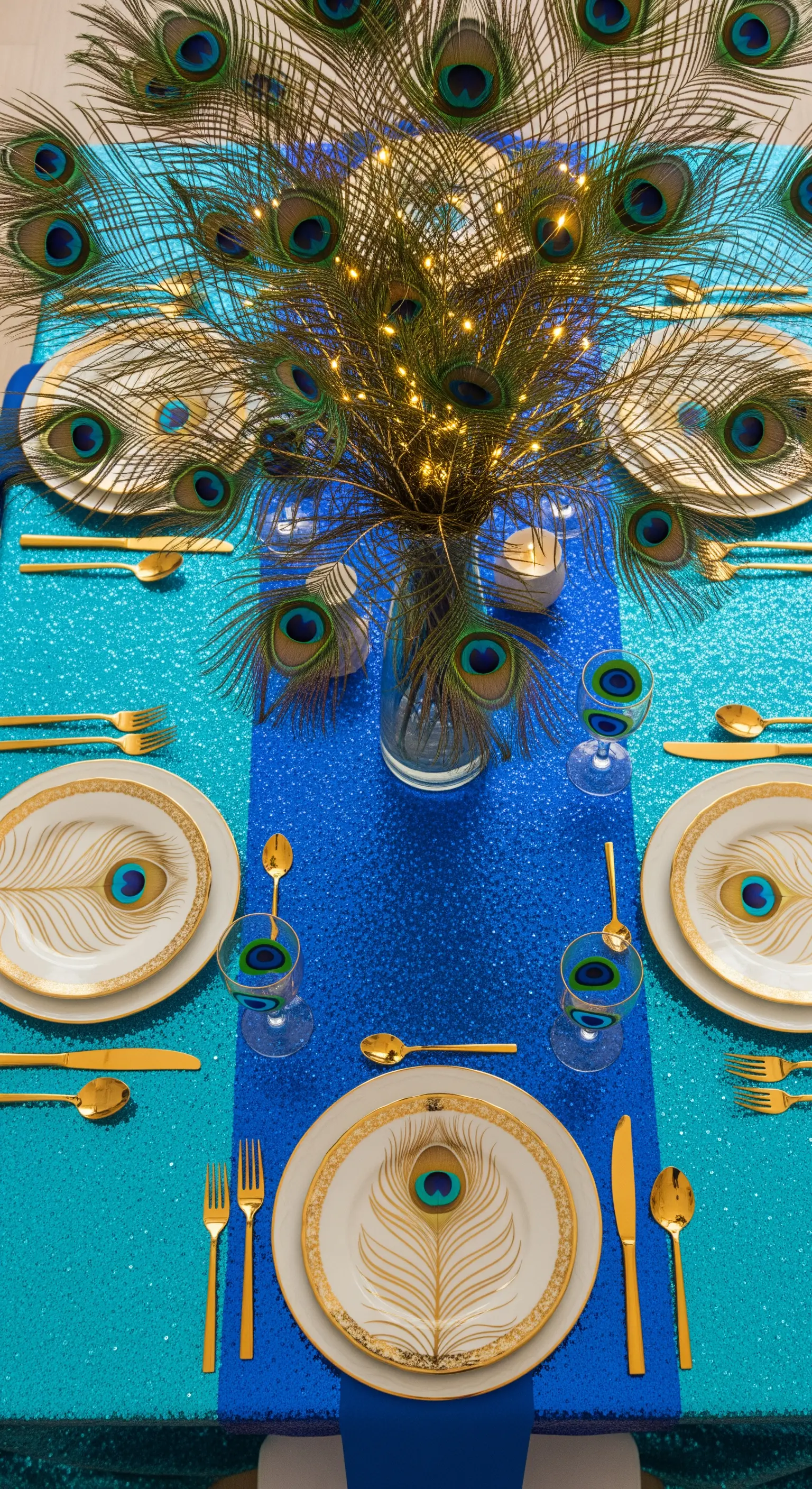 Tavola a tema pavone con piume, tovaglia blu e turchese e dettagli dorati.