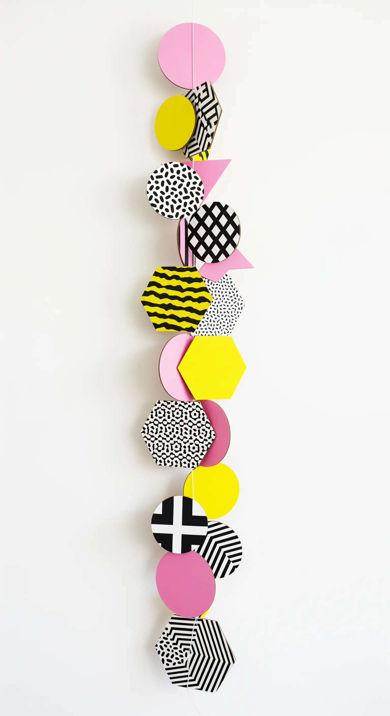 Ghirlanda verticale con forme geometriche di carta gialla, rosa e con pattern in bianco e nero.