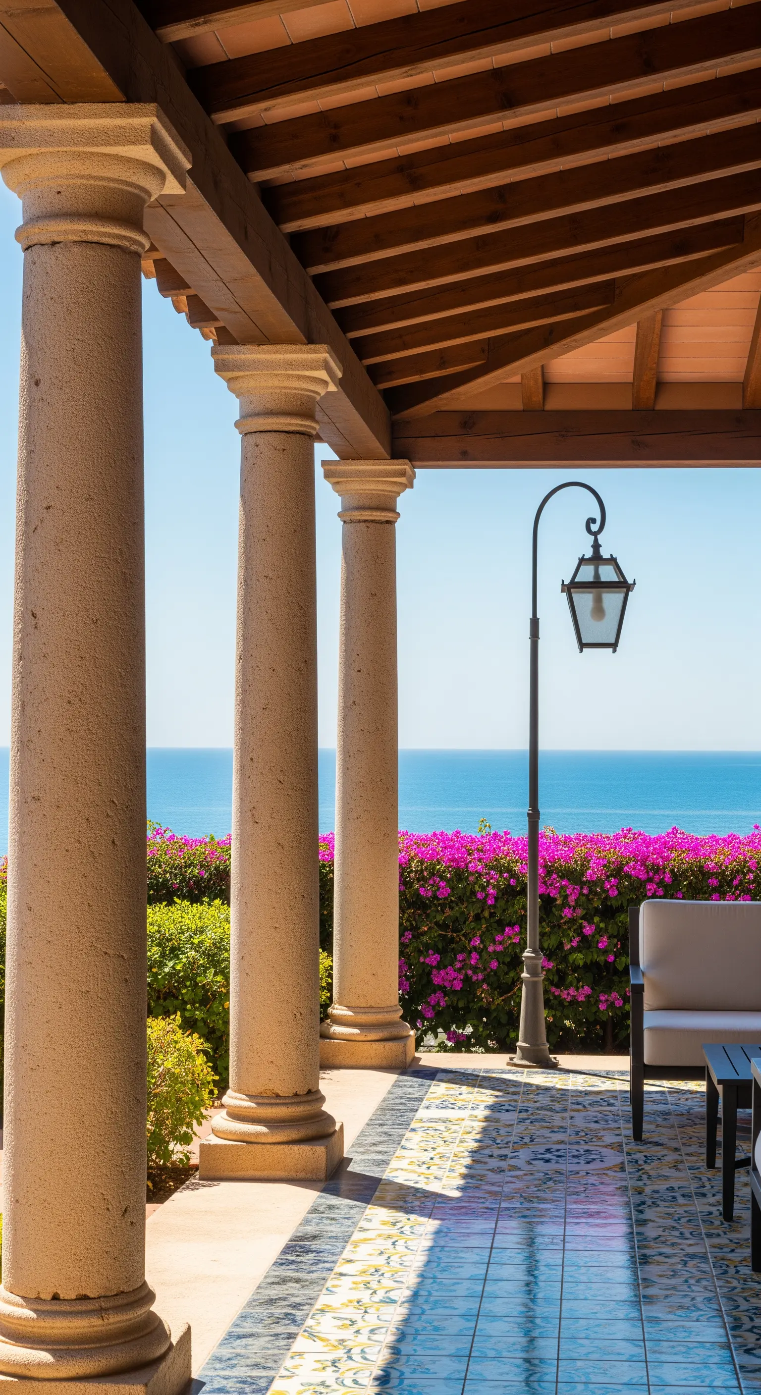 Portico con colonne in pietra grezza, pavimento in maiolica e siepe di bouganville vista mare.