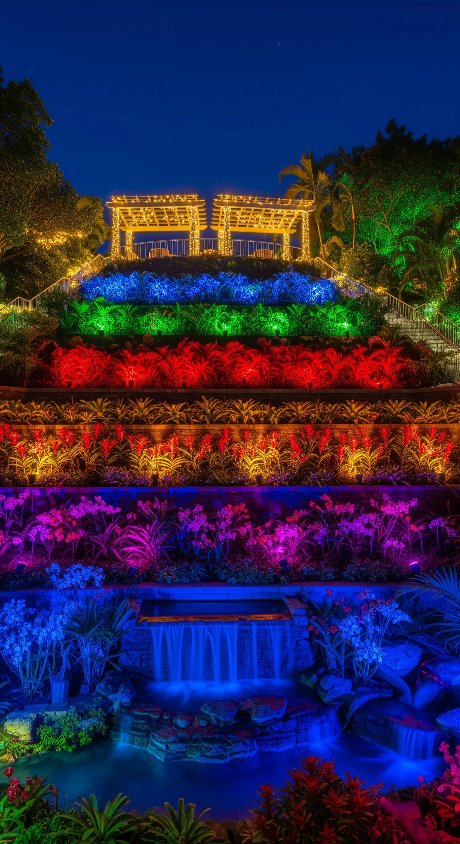 Giardino a terrazze illuminato con fasce di luce colorate: blu, viola, rosso, giallo e verde.