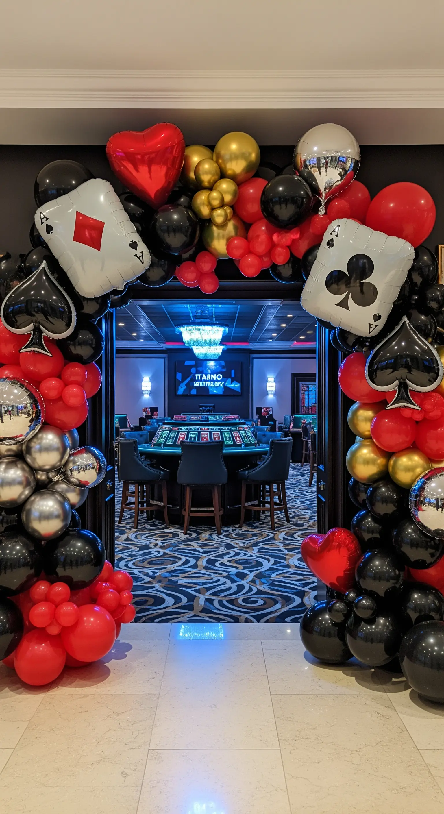 Ingresso incorniciato da un arco di palloncini rossi, neri e dorati con forme di semi delle carte.