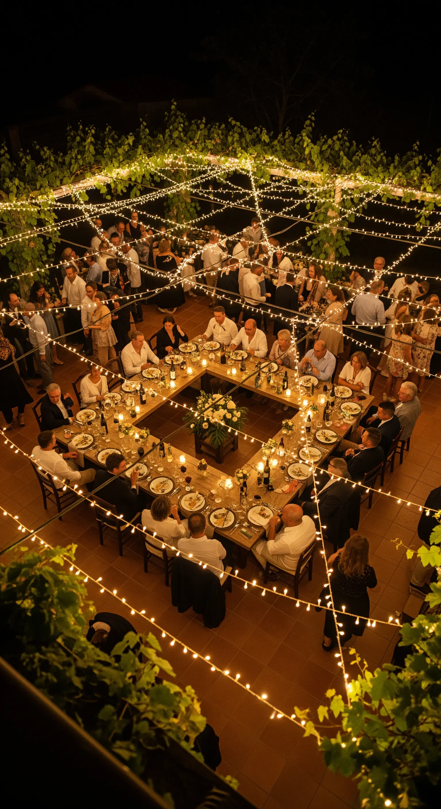 Cena all'aperto di notte con tavoli a corte sotto una cascata di lucine
