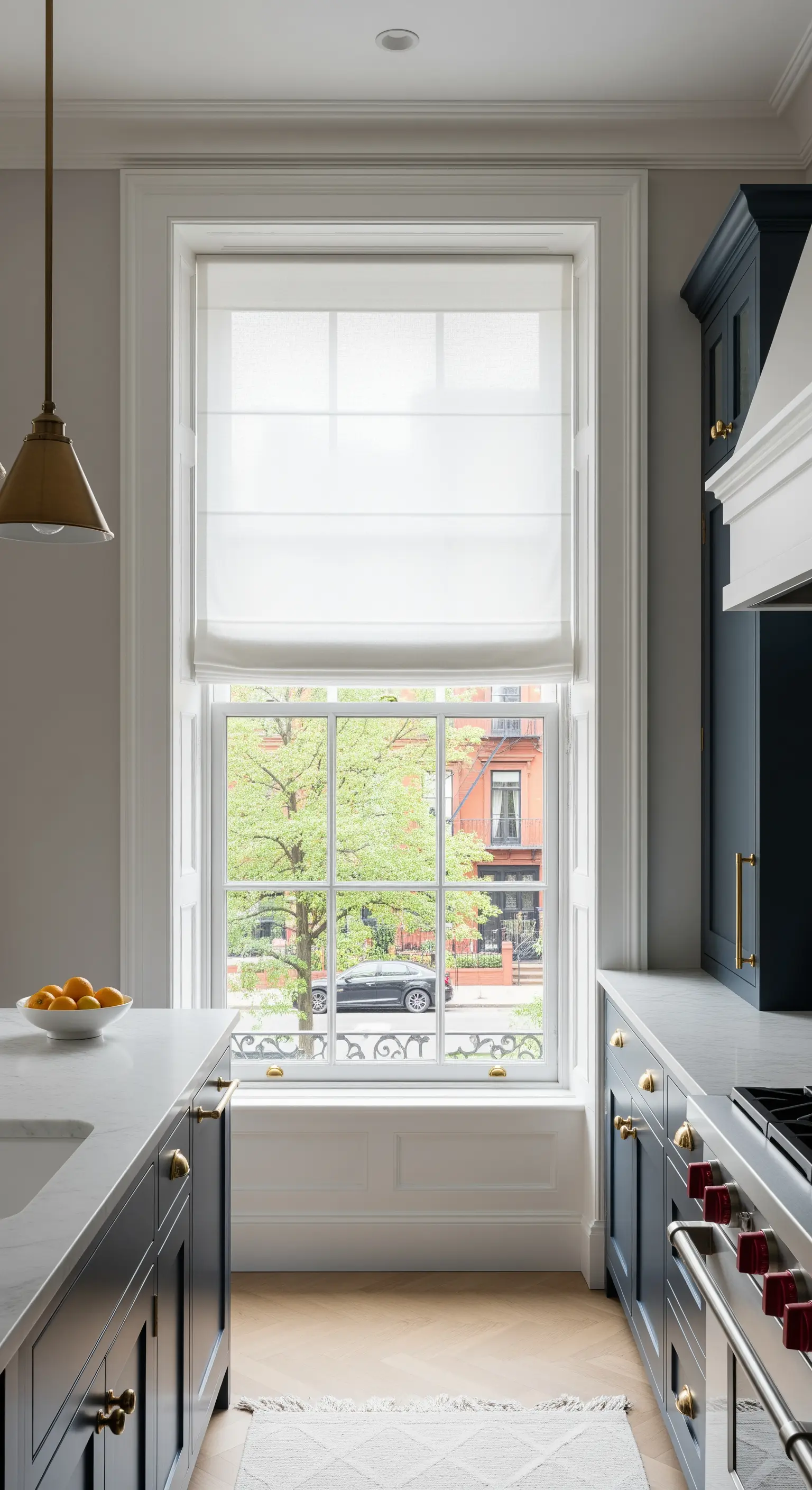 Cucina classica con mobili blu e una grande finestra con tenda a pacchetto bianca.