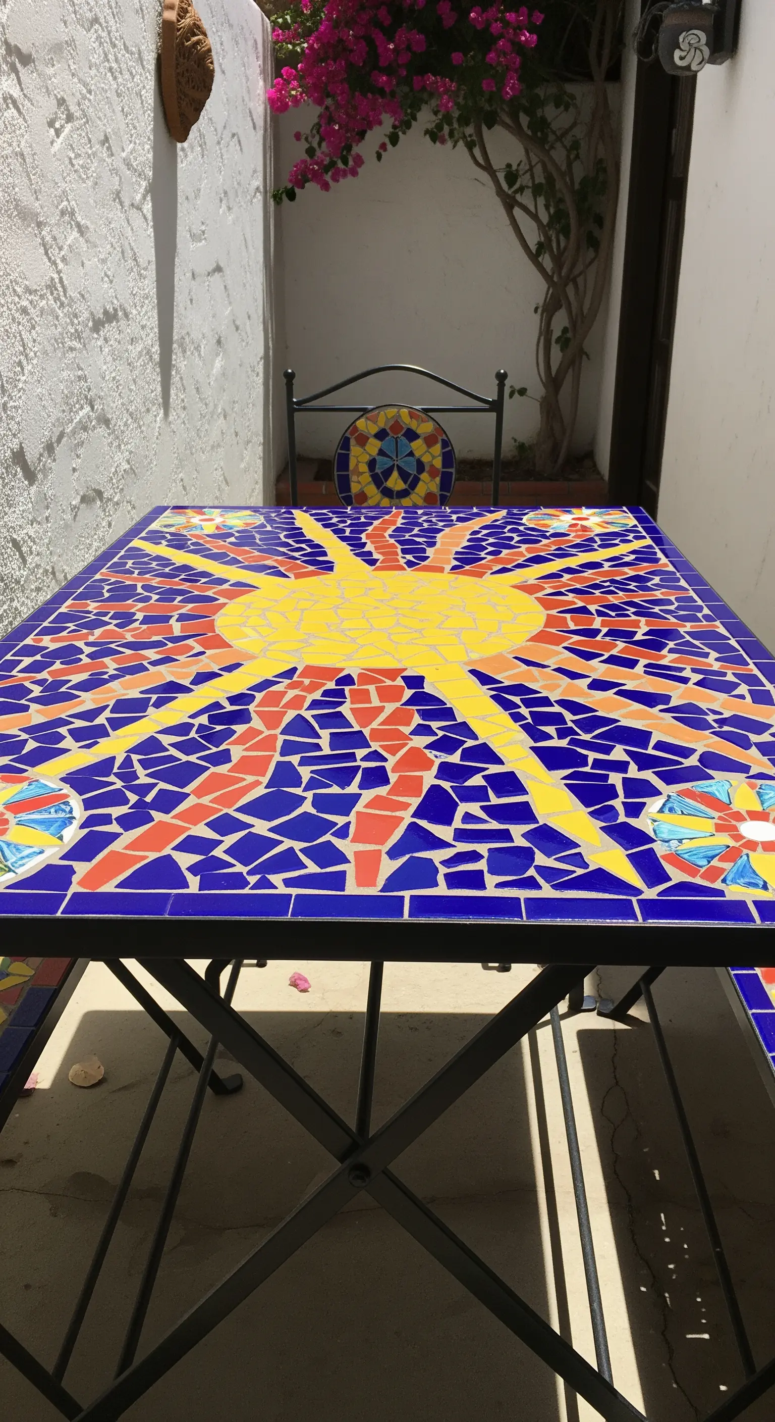 Tavolo da esterno con piano in mosaico raffigurante un sole giallo e rosso su fondo blu.