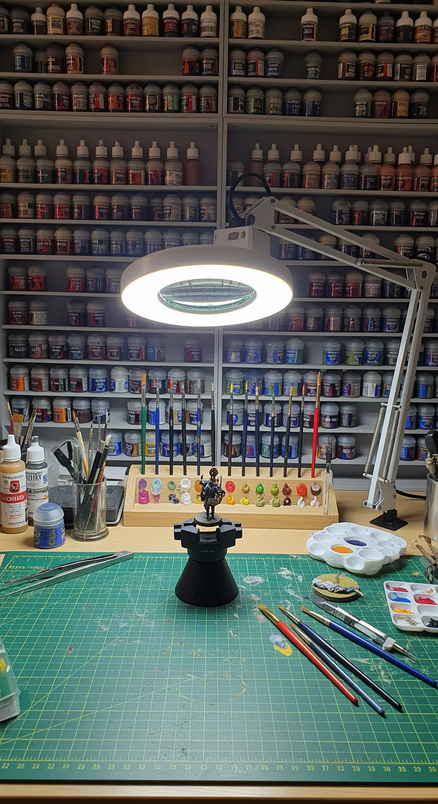 Postazione per dipingere miniature con lampada a lente circolare e centinaia di boccette di colore.