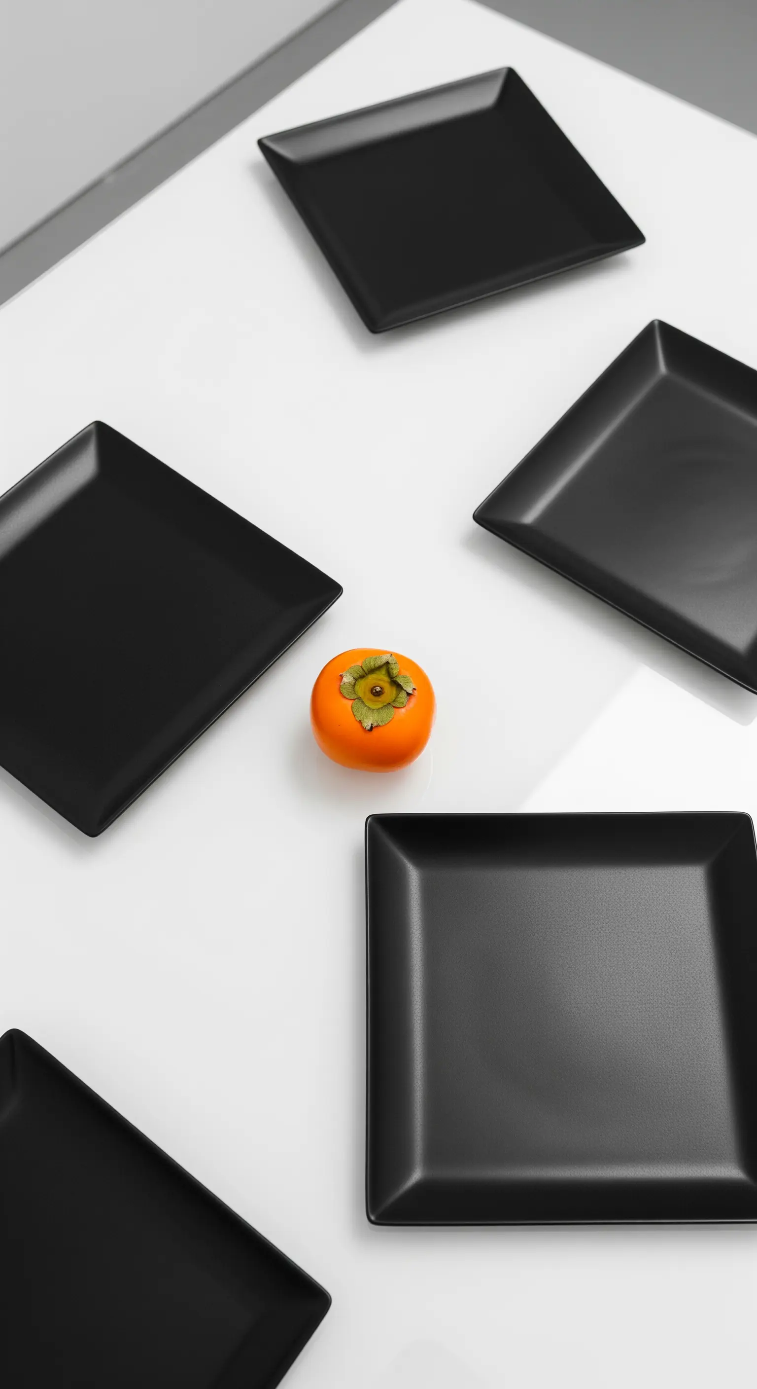 Un caco arancione al centro di una composizione di piatti neri quadrati.