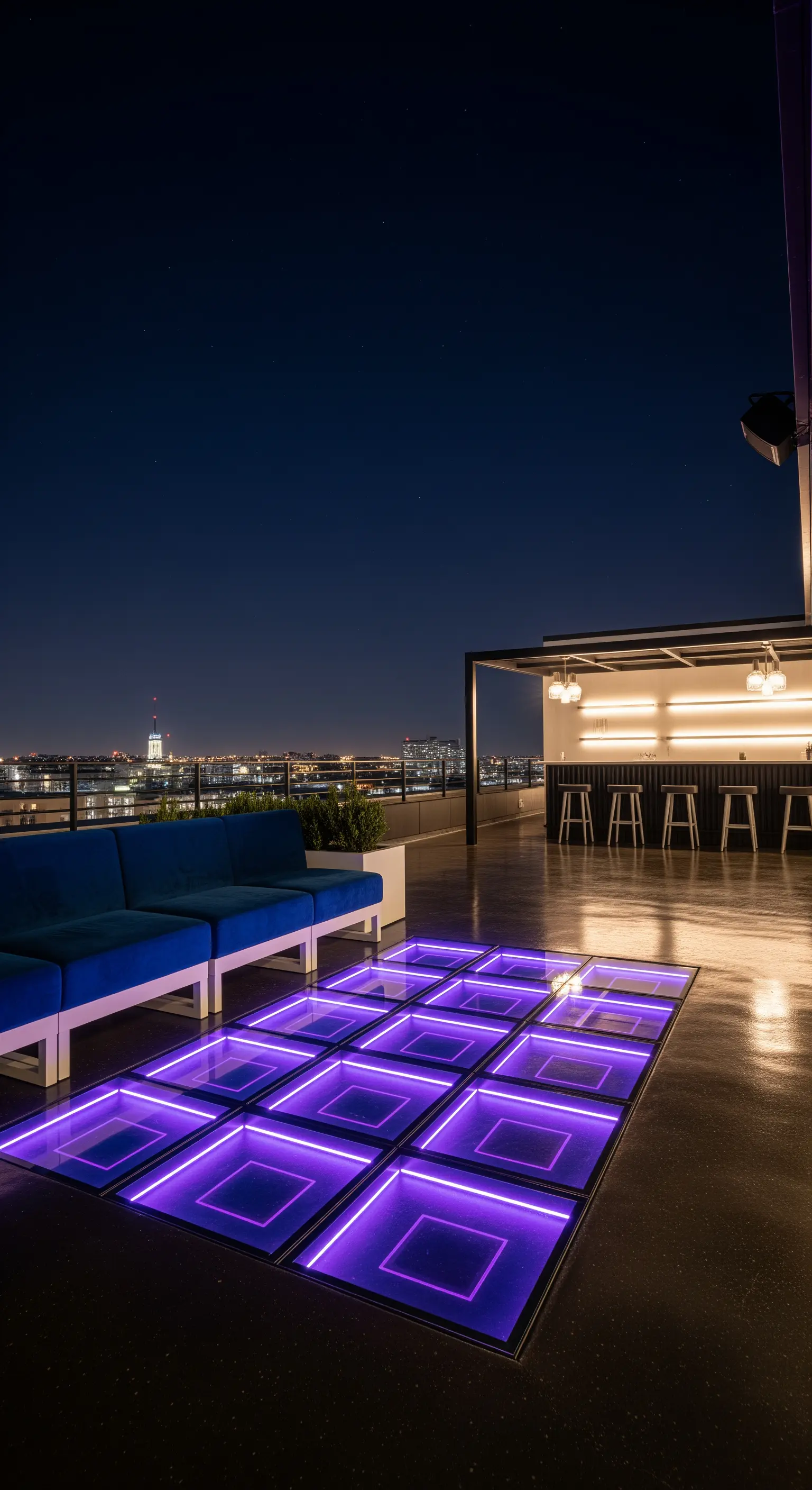 Rooftop con divano blu, bancone bar e una sezione di pavimento in vetro illuminata dal basso con luce viola
