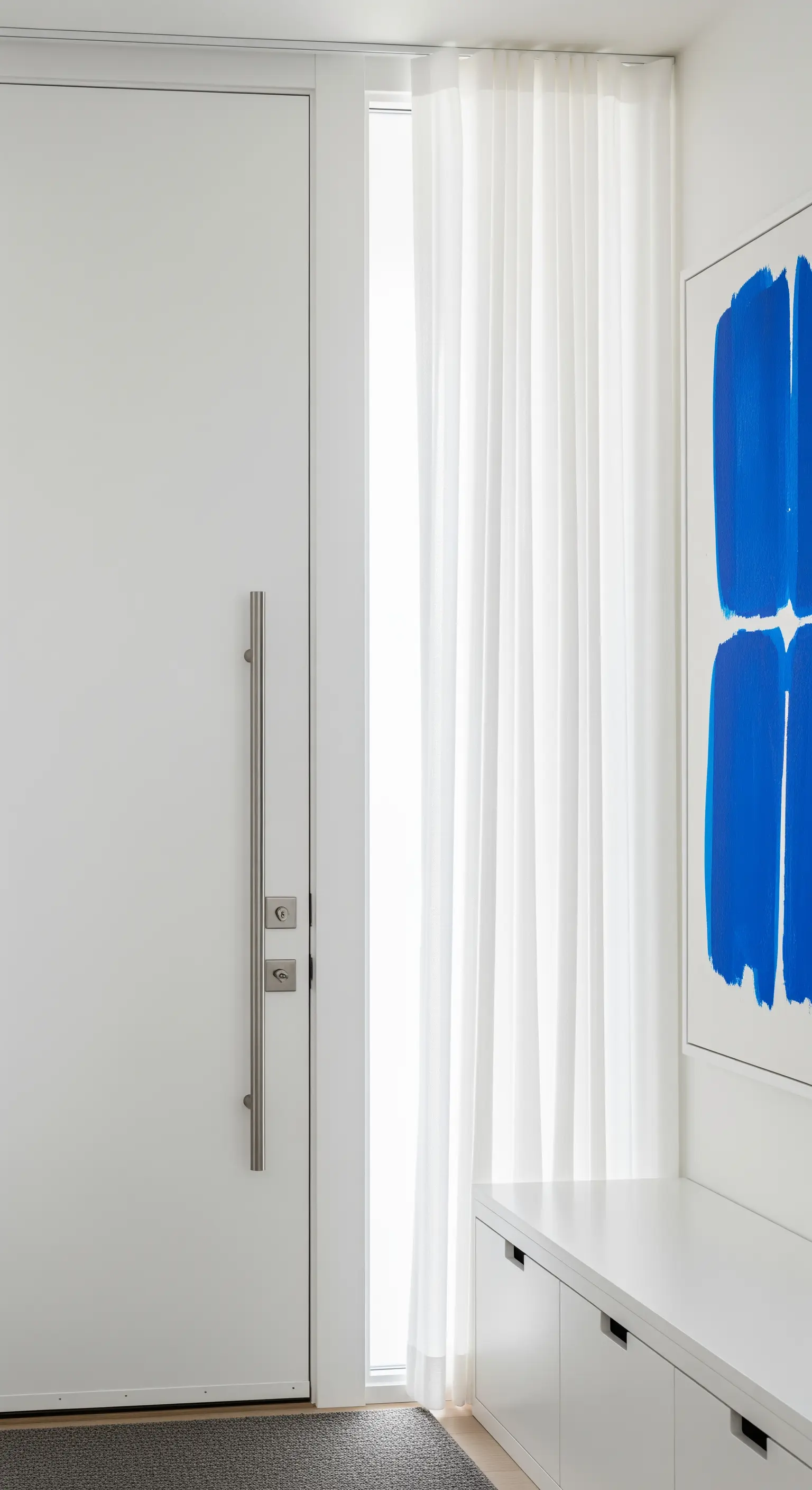 Ingresso bianco minimalista con una grande opera d'arte astratta blu e una tenda bianca a tutta altezza.