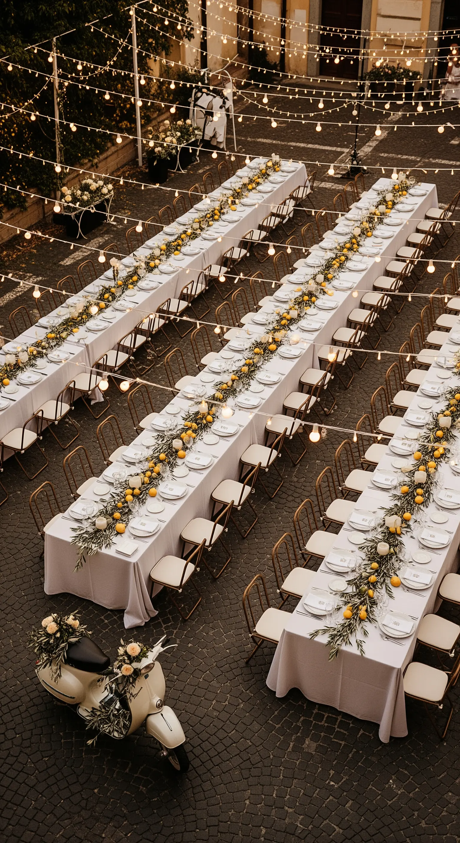 Lunghe tavolate all'aperto illuminate da lucine, con una Vespa decorata con fiori